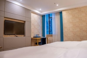 A hotel room with a bed, a TV mounted on the wall, a desk with a chair, and a window with curtains.