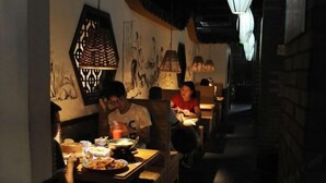Un restaurant poc il·luminat amb taules i cadires, que destaca per les obres murals i les làmpades penjants.
