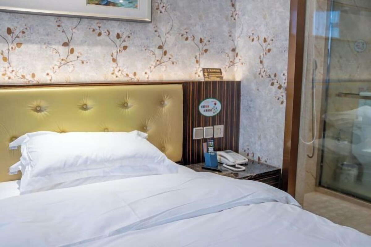 A hotel room with a bed, a bedside table with a telephone, and a wall-mounted clock.