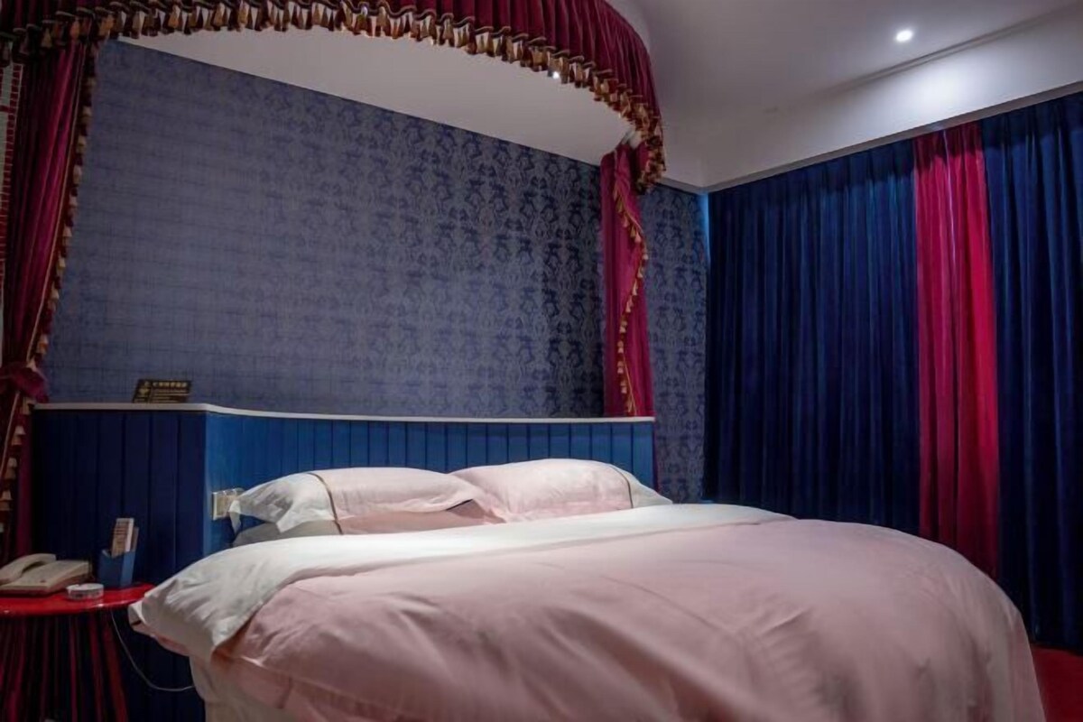 A hotel room with a large bed, a bedside table with a telephone, and a curtain with a gold trim.
