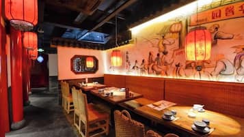 Interior de restaurante con mesas y sillas de madera, faroles rojos y un mural en la pared.
