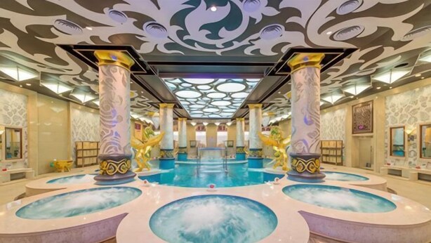 A large indoor swimming pool with multiple circular water features, ornate columns, and a decorative ceiling. - Yinhehui Hotel (Changchun Railway Station Sasseur Zhongdong Outlet) (Changchun)