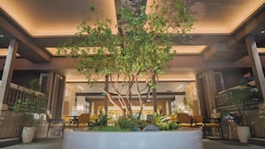 An indoor atrium with a central tree, seating areas, and a modern ceiling design. - Yinhehui Hotel (Changchun Railway Station Sasseur Zhongdong Outlet) (Changchun)