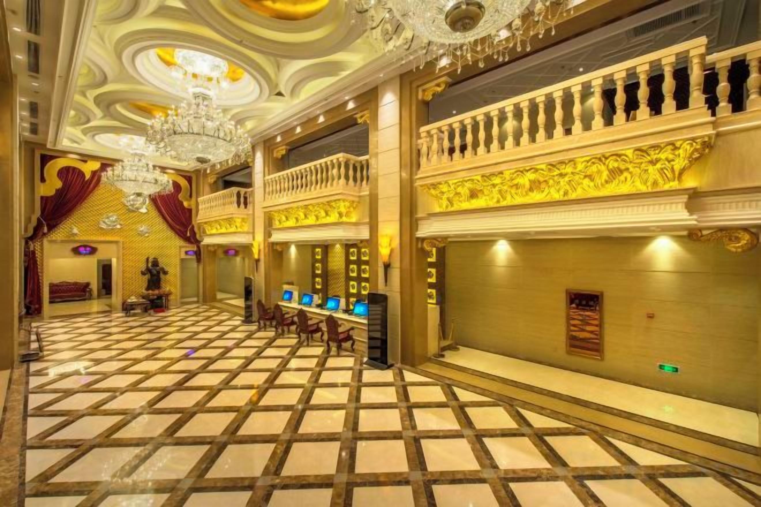A grand hotel lobby with a checkered floor, chandeliers, and a balcony with ornate railings.