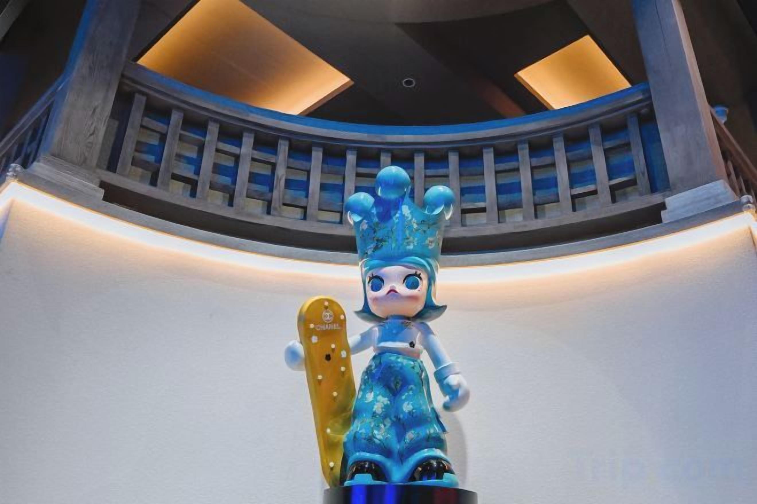 A figure with a crown and a snowboard in a room with a curved ceiling and a balcony.