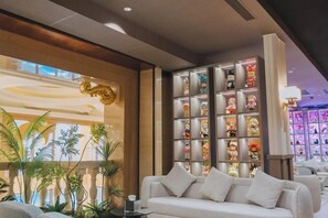 A hotel lobby with a white sofa, a decorative wall with figurines, and a plant arrangement. - Yinhehui Hotel (Changchun Railway Station Sasseur Zhongdong Outlet) (Changchun)