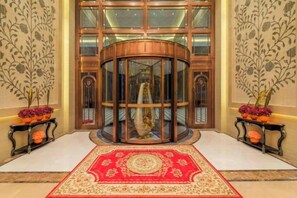 A hotel lobby with a central revolving door, a red patterned carpet, and two side tables with potted plants. - Yinhehui Hotel (Changchun Railway Station Sasseur Zhongdong Outlet) (Changchun)