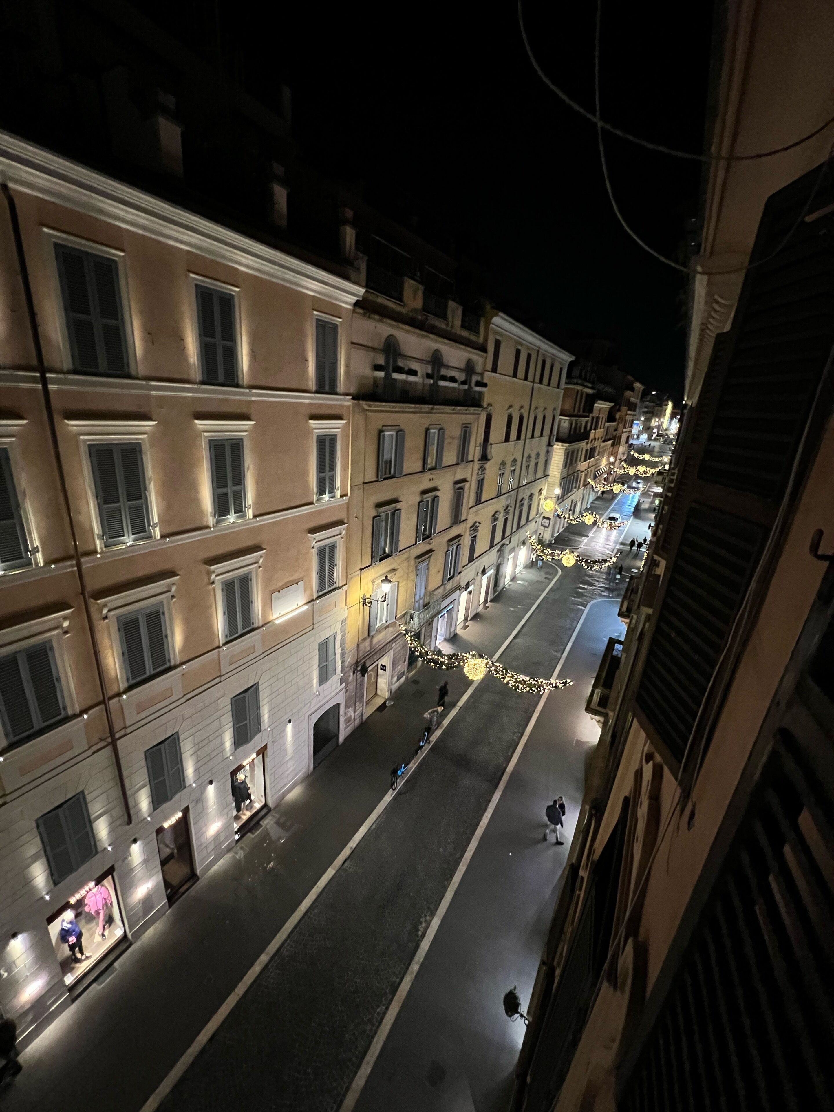 A nighttime street view with buildings on either side, illuminated by street lamps and shop lights.
