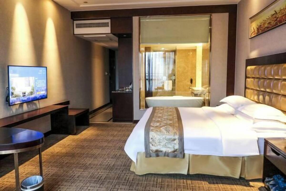 Una habitación de hotel con cama, escritorio, televisor y aire acondicionado.