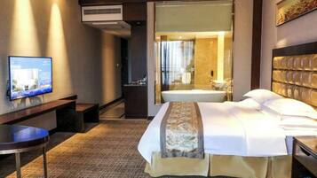 A hotel room with a bed, a desk, a television, and an air conditioning unit.
