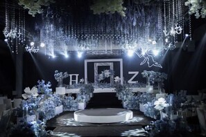 A stage with a circular platform, surrounded by floral arrangements and hanging lights.