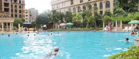 A swimming pool surrounded by buildings with arched windows, some greenery, and lounge chairs.