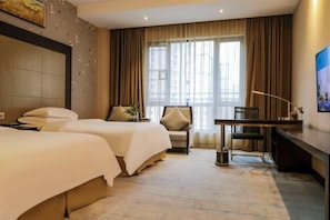 Habitació d'hotel amb dos llits, una taula de treball, una cadira i una finestra gran amb cortines.