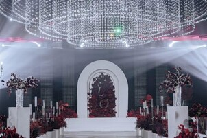 Un escenario con un arco blanco y adornos florales, rodeado de pilares blancos.