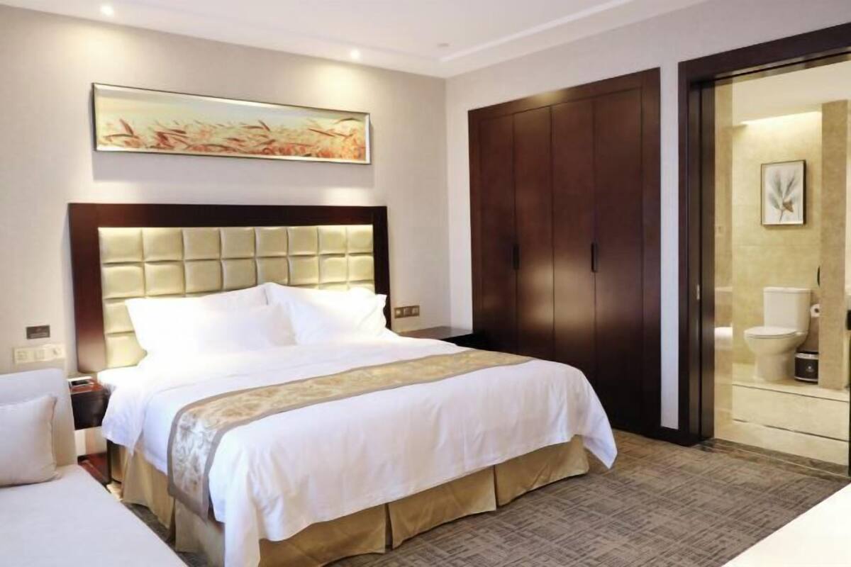Una habitación de hotel con una cama grande, un armario de madera y un baño con inodoro y lavabo.