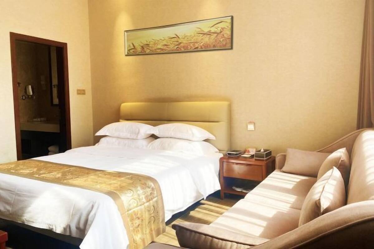 Una habitación de hotel con una cama, un sofá, una mesita de noche y un cuadro en la pared.