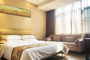 Habitació d'hotel amb llit, sofà, quadre a la paret i finestra amb cortines.