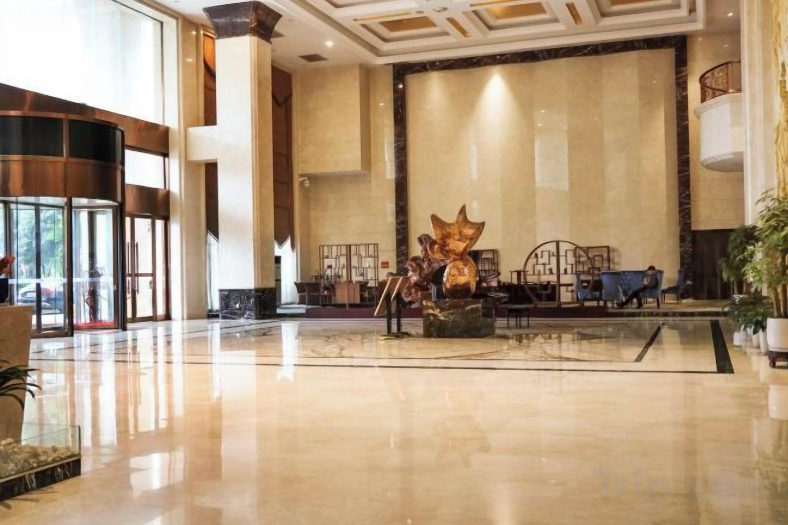 A spacious lobby with a large reception desk, a decorative sculpture, and a seating area with tables and chairs.