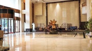 A spacious lobby with a large reception desk, a decorative sculpture, and a seating area with tables and chairs.