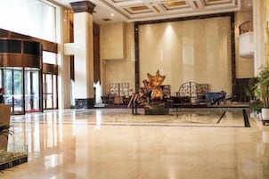 Un vestíbulo amplio con un mostrador de recepción grande, una escultura decorativa y una zona de estar con mesas y sillas.