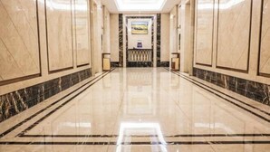 En hotellkorridor med polerade marmorgolv och -väggar, ett centralt placerat konstverk och ett dekorativt räcke.