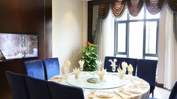 A dining area with a round glass table, blue upholstered chairs, and a large window with curtains.