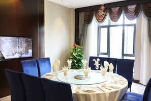 A dining area with a round glass table, blue upholstered chairs, and a large window with curtains.