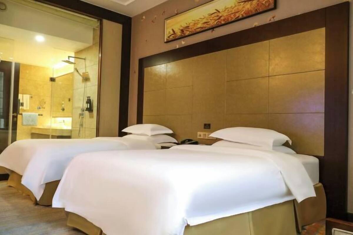 Habitación de hotel con dos camas, un espejo grande y zona de ducha.