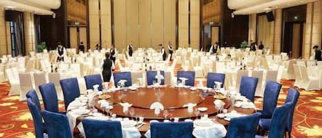 Une salle de conférence avec une table ronde entourée de chaises bleues, de tables blanches et d’un sol recouvert d’une moquette rouge.