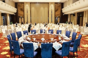 A conference room with a round table surrounded by blue chairs, white tables, and a red carpeted floor.