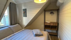 A bedroom with a sloped ceiling, a bed with a patterned bedspread, a hanging light fixture, and a small wooden shelf. - Cozy apartment for your family. (RS)