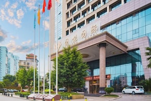 A modern building with a prominent entrance, multiple flags, and a clear sky. - Guoneng Grand Hotel (Dianjiang County)