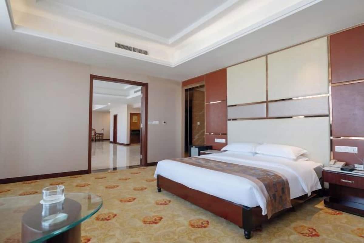 A hotel room with a bed, a bedside table, a mirror, and a glass table with a clear glass.