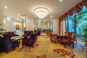 Un hall d’hôtel agrémenté d’un lustre, d’un espace salon et de grandes fenêtres.