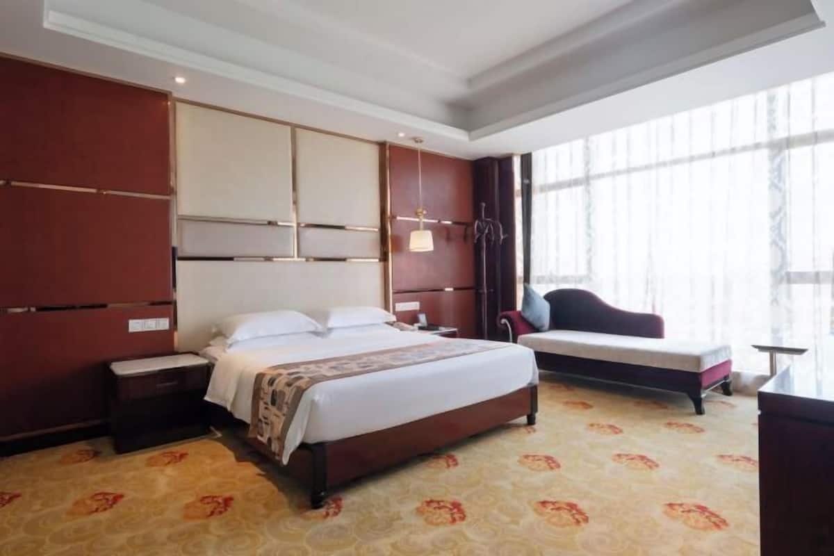 A hotel room with a large bed, a bedside table, a chair, a desk, and a window with curtains.
