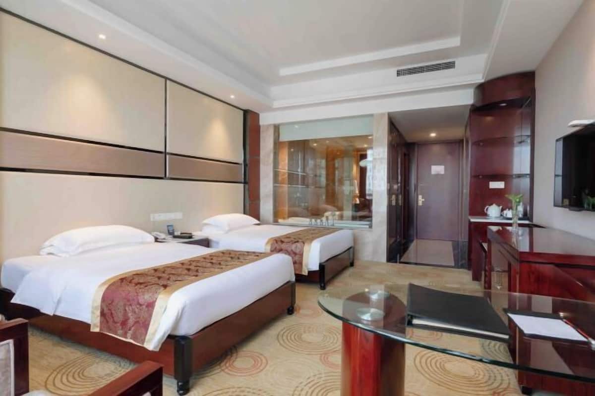 A hotel room with two beds, a glass coffee table, a desk, and a mirror.