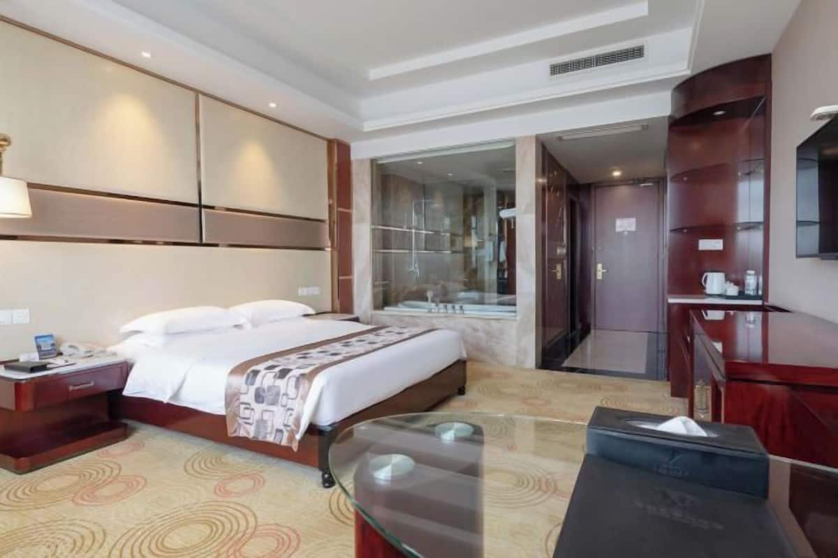 A hotel room with a bed, bedside table, lamp, and a glass coffee table.