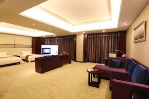 Quarto de hotel com uma cama grande, um sofá, uma televisão e uma secretária com um computador.