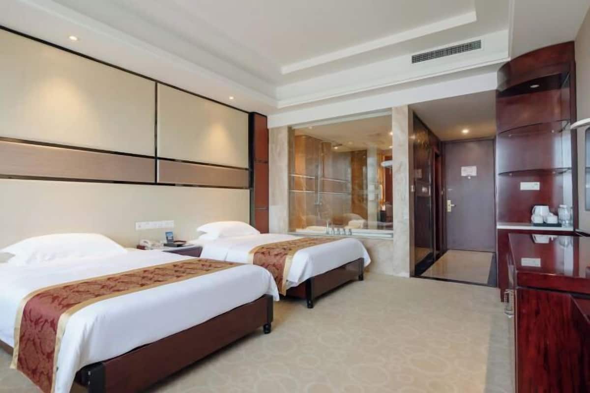 A hotel room with two beds, a large mirror, a wardrobe, and a bathroom visible through an open door.