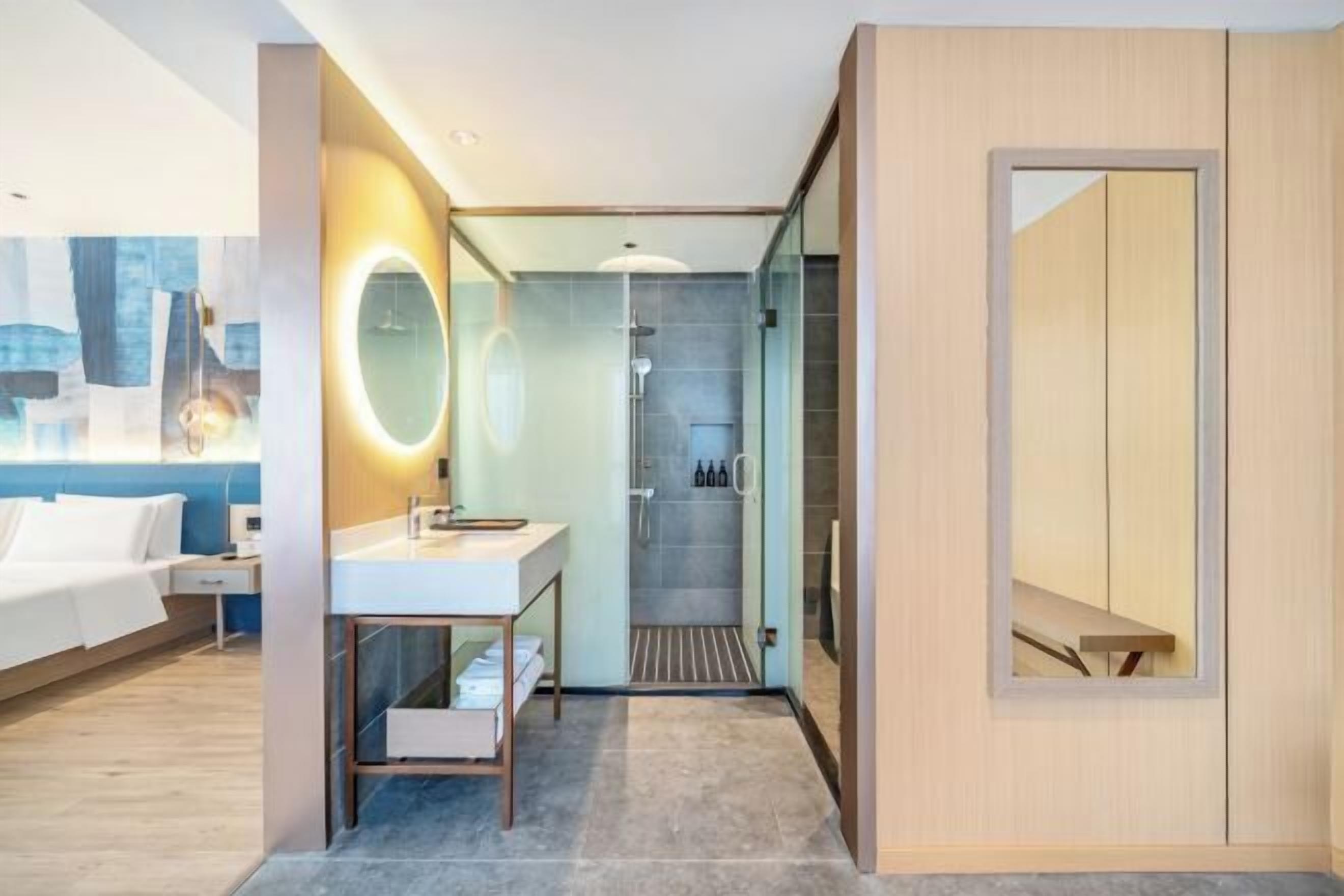 Habitación de hotel moderna con cama, tocador con espejo, ducha y vista panorámica de la ciudad.