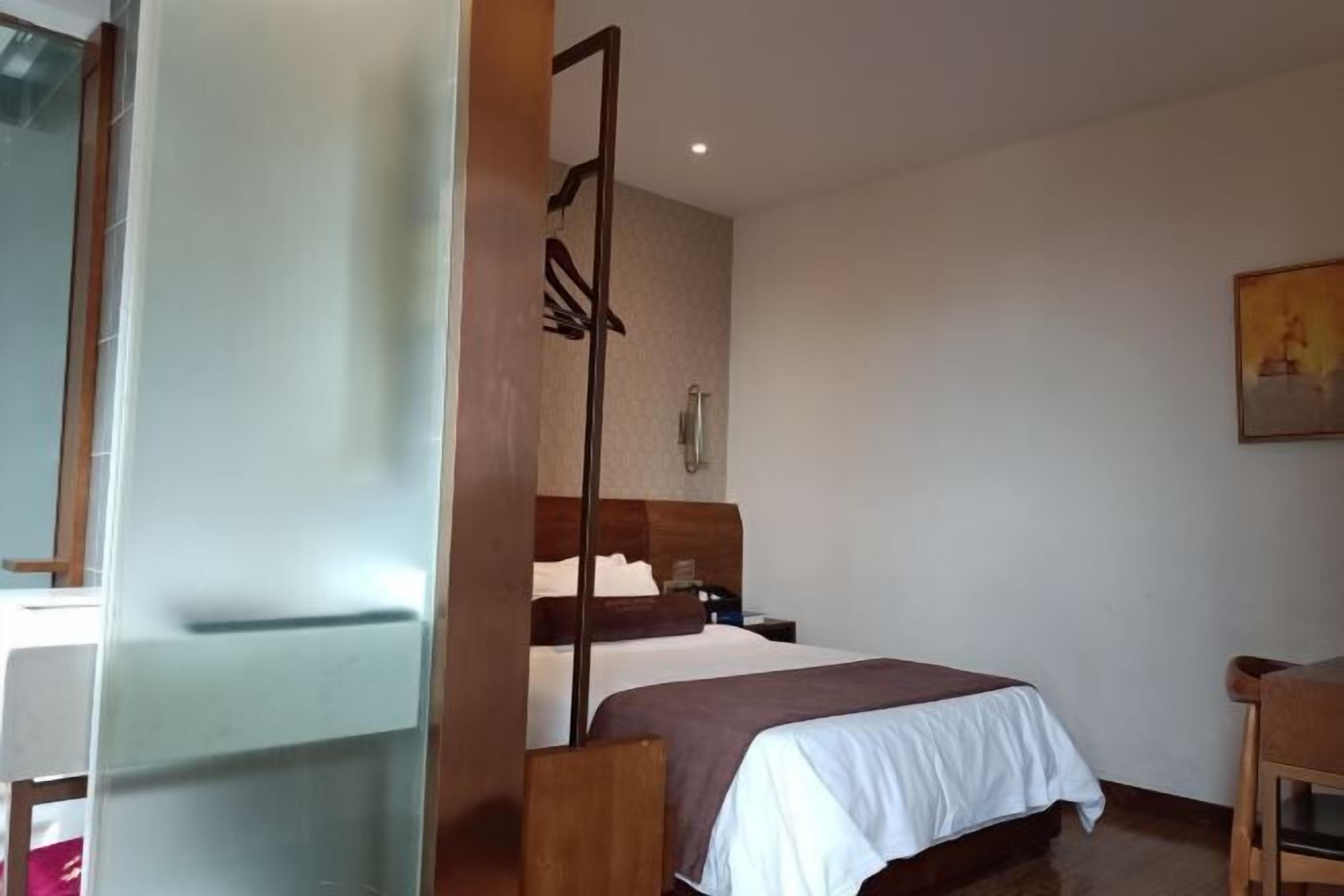 A hotel room with a bed, a wooden headboard, a nightstand, and a chair.