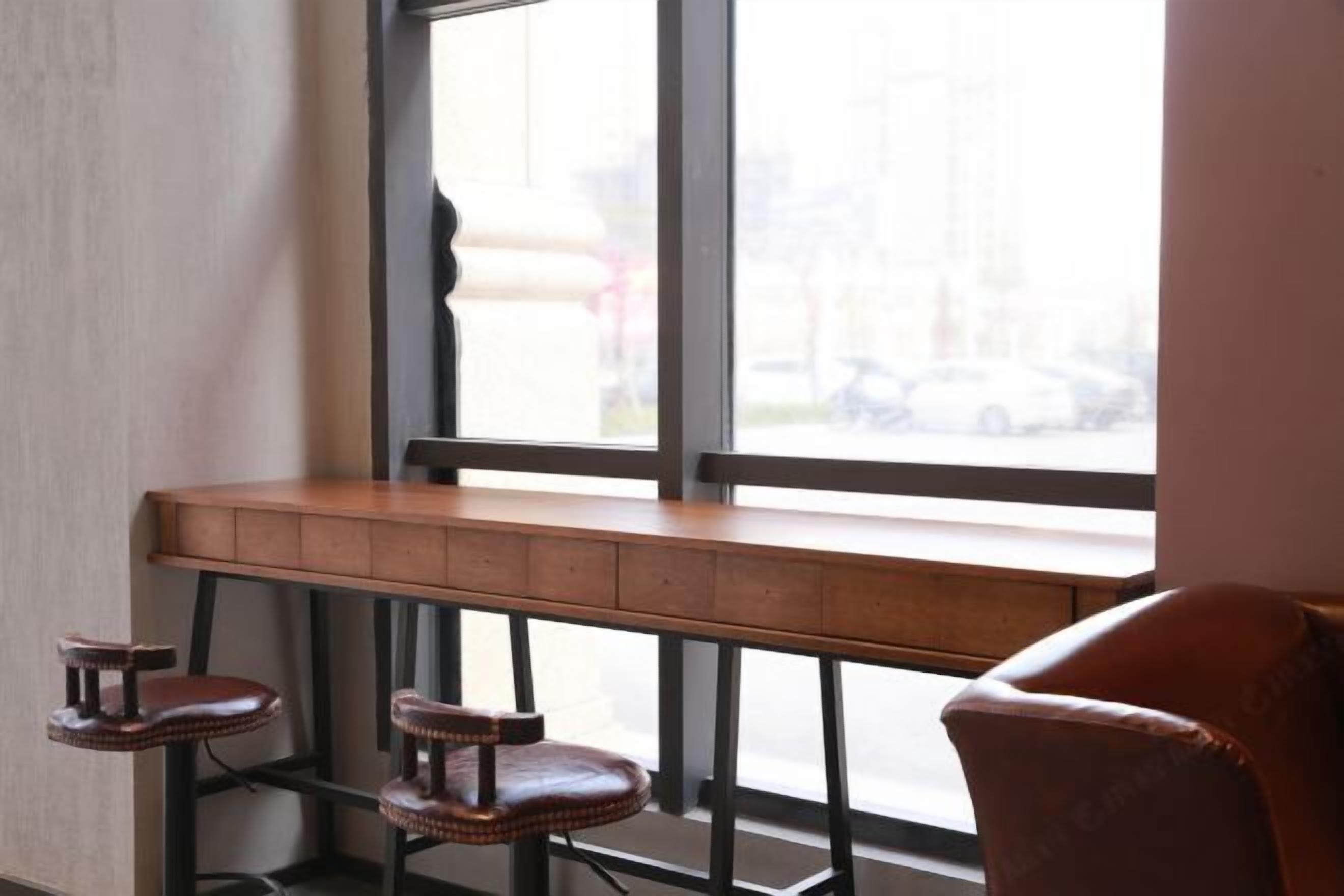 Un espace bar avec un banc et des tabourets en bois, et une grande fenêtre donnant sur la rue.
