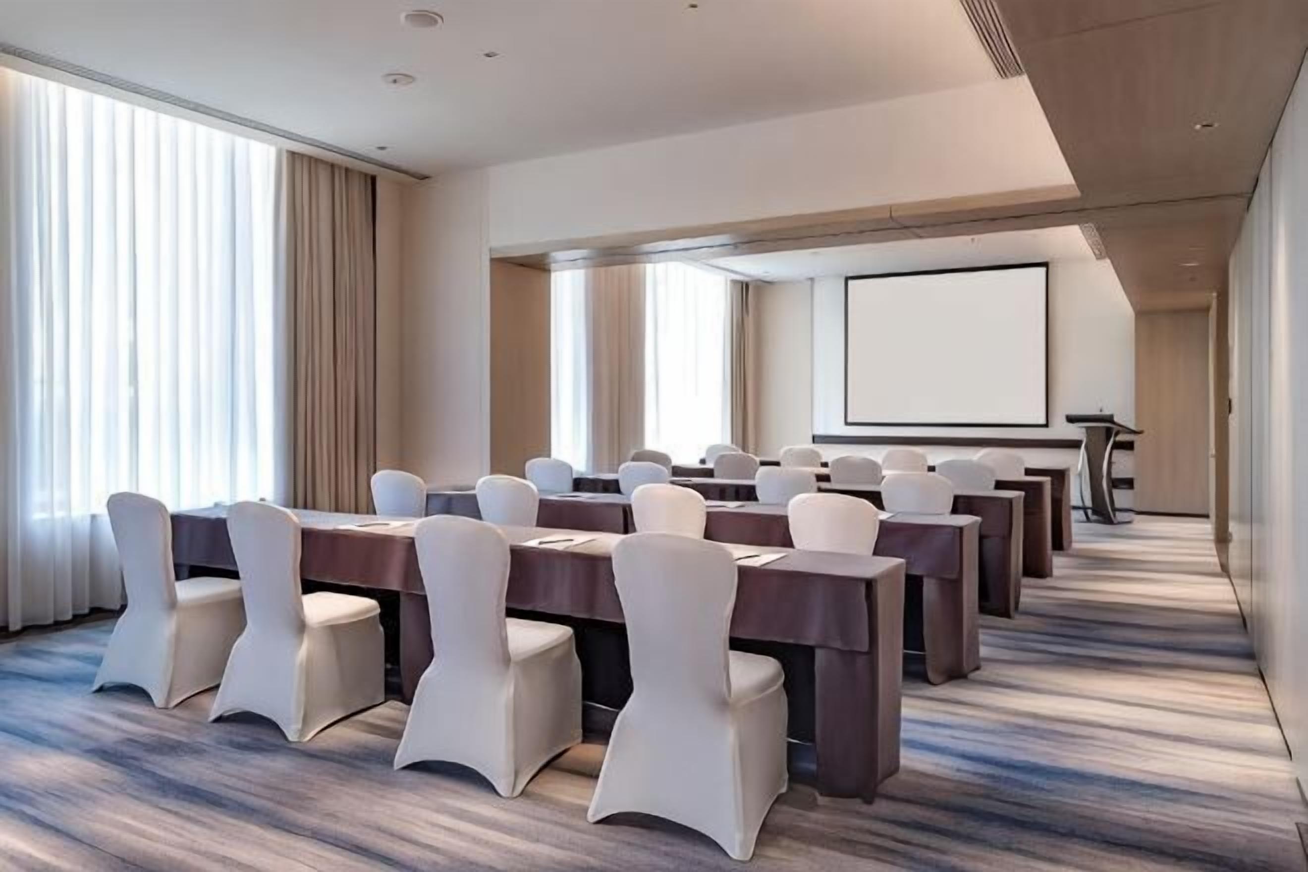 Un salón de conferencias con una larga mesa, sillas, una pantalla de proyector y un amplio ventanal.