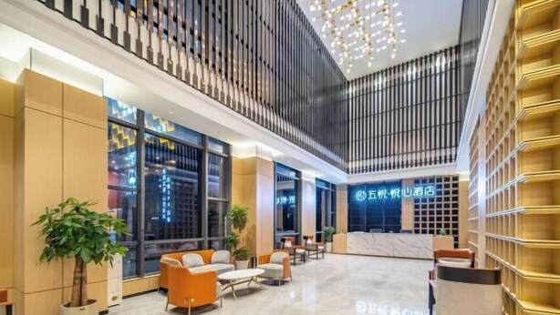 A hotel lobby with seating areas, a reception desk, and large windows offering city views.