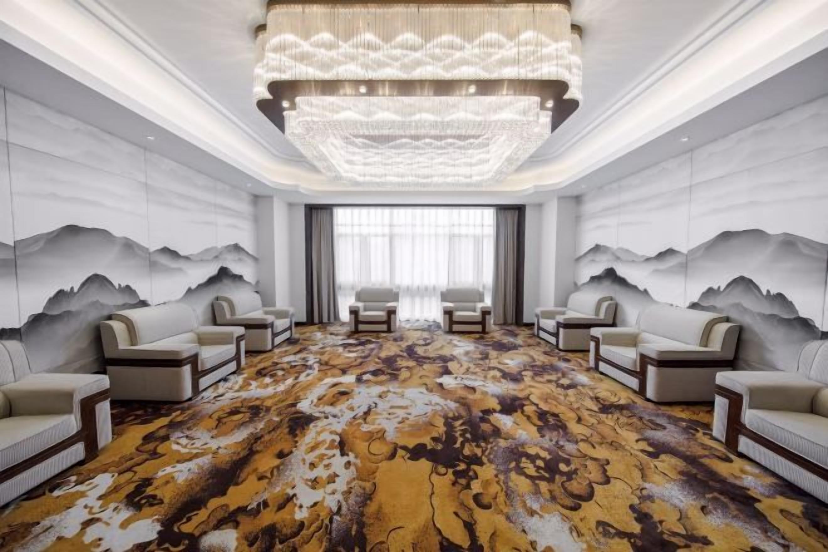 A spacious room with a large carpet, two sofas, a chandelier, and a wall with mountain paintings.