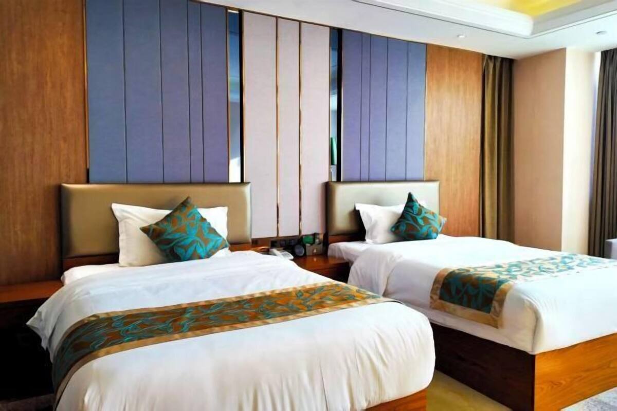 A hotel room with two beds, wooden headboards, and a large window.