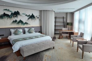 A modern hotel room with a large bed, a seating area with a table, and a view of the outdoors.