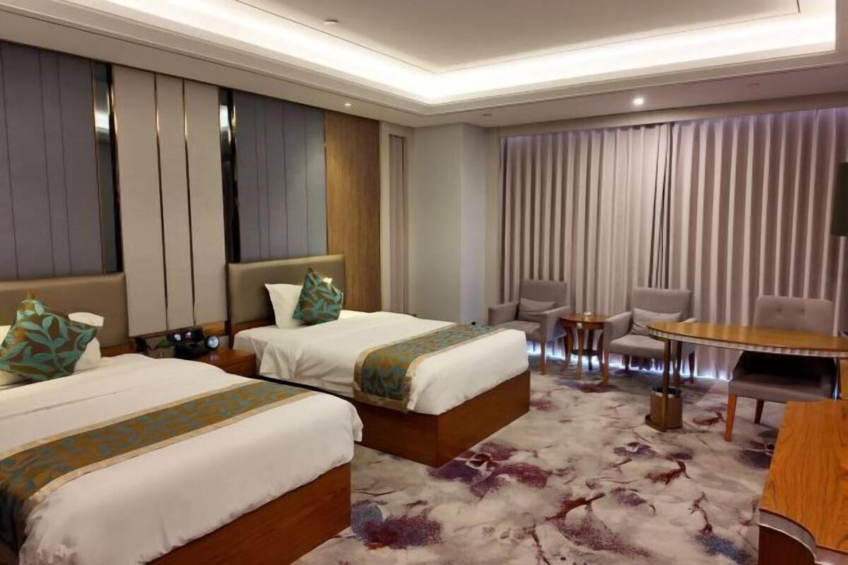 A hotel room with two beds, a small seating area, and a large window with curtains.