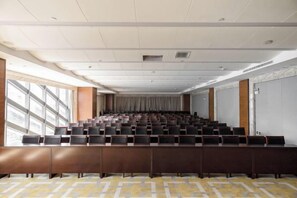 A conference room with rows of chairs, a carpeted floor, and large windows on one side.