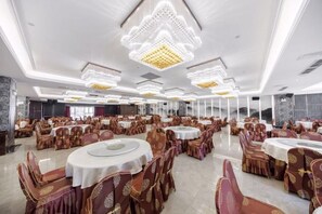 A banquet hall with round tables and chairs, high ceiling with chandeliers, and a polished floor. - Bai Rui Sheng Hotel (Huaping)